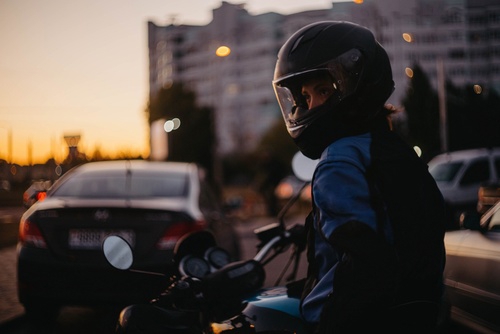 Female motorcyclist riding motorcycle on city street wearing helmet and protective jacket