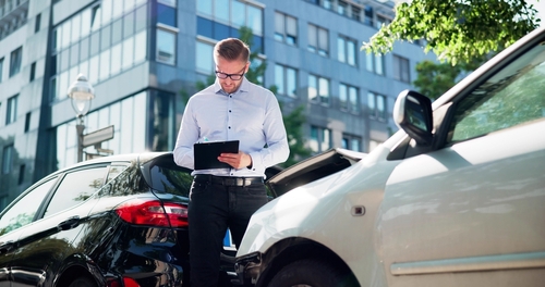 Man holding clipboard examines damaged cars parked on city street