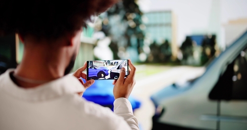 insurance adjuster photographing vehicle collision damage with smartphone at accident scene