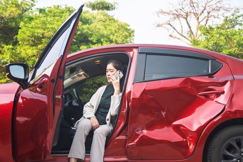 woman sitting in damaged car with open door talking on phone