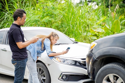 woman photographing vehicle collision damage with smartphone while man stands nearby